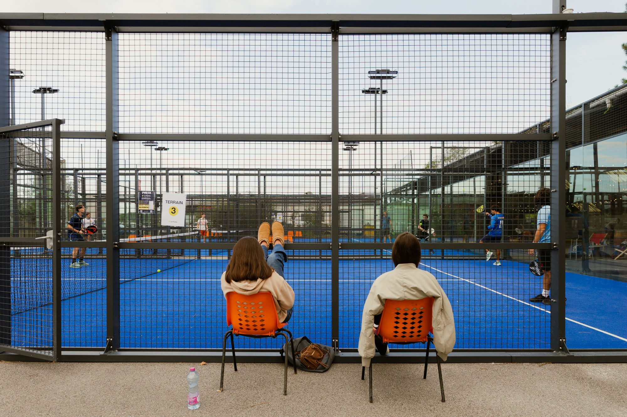 Deux spectateurs assis face à un terrain de padel du Punto